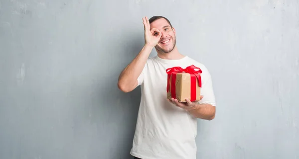 Young Caucasian Man Grey Grunge Wall Holding Present Happy Face — Stock Photo, Image