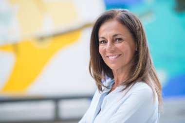 Street yüzünde gülümseme ile duran güzel orta yaş İspanyol kadın. Şehrin içinden süre gülümseyen güneşli bir günde kendine güvenen ve neşeli yürüyüş.