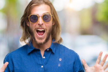 Üzerinde güneş gözlüğü takmış uzun saçlı yakışıklı delikanlı deli kutluyor arka plan izole ve silah ile başarı için yükseltilmiş ve açık gözleri heyecanlı çığlık hayrete düşürdü. Kazanan kavramı