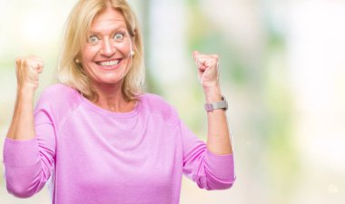 Gülümseyen ve başarı için çığlık orta yaş sarışın kadın izole arka plan çok mutlu ve heyecanlı kaldırdı, silah ile kazanan jest yapıyor. Kutlama kavramı.