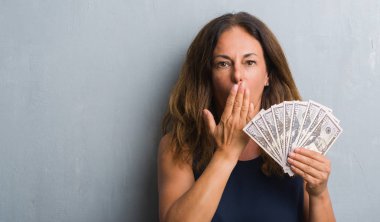 Dolar kapağı ağız el hata, korku, sessizlik içinde gizli kavramı korkmuş ifade için utanç ile şok ile tutarak gri grunge duvarın üzerinden duran orta yaş İspanyol kadın