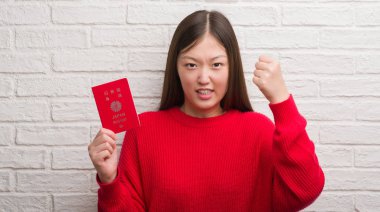 Genç Çinli kadın üzerinde tuğla duvar holding pasaport Japonya rahatsız ve boşa çıkarmak ile öfke, çılgın ve yükseltilmiş eliyle diye bağıran öfke kavramı bağırarak.