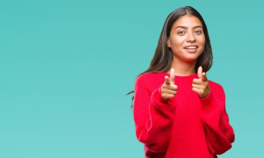 Fotoğraf makinesi ile mutlu ve komik yüz için parmakları işaret izole arka plan üzerinde kış kazak giyen genç güzel Arap kadın. İyi enerji ve vibes.