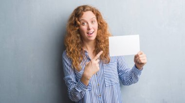 Gri grunge duvar boş kartı çok mutlu el ve parmak ile işaret tutan genç Kızıl saçlı kadın