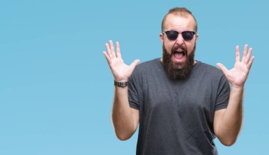 Genç beyaz hipster adam kızgın ve silah ile başarı için deli izole arka plan kutluyor üzerinde güneş gözlüğü takıyor kaldırdı ve heyecanlı çığlık gözler kapalı. Kazanan kavramı