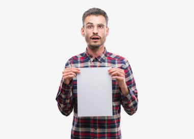 Genç yenilikçi yetişkin adam holding boş kağıt sayfası bir sürpriz yüz, korkuyor ve heyecanlı korku ifadesi ile şok korkmuş