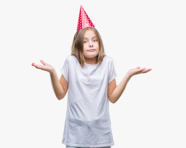 Genç güzel kız Doğum günü şapkası üzerinde arka plan clueless ve şaşkın bir ifadeyle kollar ve eller kaldırdı izole. Şüphe kavramı.