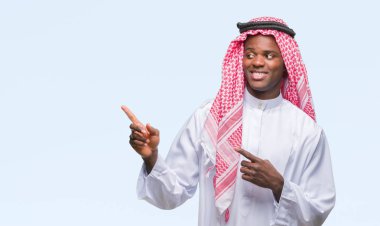 Gülümseyen ve iki elleri ve parmakları ile tarafına işaret kamera bakarak izole arka plan üzerinde geleneksel keffiyeh giyen genç Arapça Afrika adam.