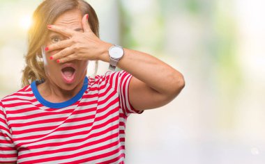 Mahcup ifadeyle parmaklarımın arasından seyir orta yaş İspanyol kadın kıdemli yüz ve gözler el ile kapsayan şok bakmak izole arka plan üzerinde.