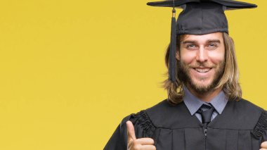 El ile pozitif jest yapıyor izole arka plan başarı işareti üzerinde uzun saçlı Genç mezun yakışıklı başparmak gülümseyen ve mutlu. Neşeli bir ifadeyle, kazanan jest kameraya bakıyor.