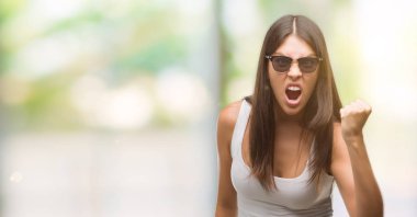 Genç güzel İspanyol giyen güneş gözlüğü kızgın ve kızgın yetiştirme hayal kırıklığı ve öfke ile bağırarak süre öfkeli yumruk. Öfke ve agresif kavramı.