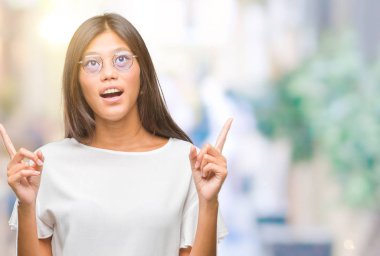 Hayret ve yukarıya bakıyor ve parmakları ile işaret ve silah kaldırdı sürpriz izole arka plan üzerinde gözlüklü Genç Asyalı kadın.