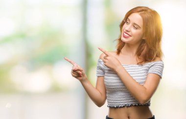 Gülümseyen ve iki elleri ve parmakları ile tarafına işaret kamera bakarak izole arka plan üzerinde genç güzel kadın.