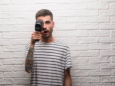 Genç adam beyaz tuğla duvarın bir sürpriz yüz, korkuyor ve heyecanlı korku ifadesi ile şok korkmuş üzerinden ayakta tutan video kamera çekimi