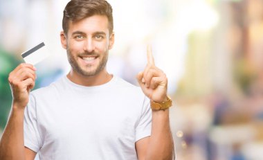 Yakışıklı delikanlı holding kredi izole arka bir fikirle sürpriz üzerinden kartı veya gülen yüz, bir numara ile işaret parmağı soru