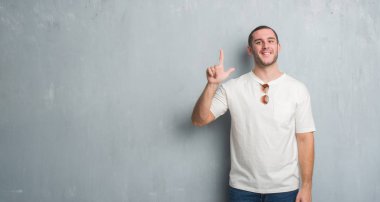 Beyaz delikanlı gösterilen ve parmakları ile işaret güneş gözlüğü takıyor gri grunge duvarın üzerinden ikincisi ise kendinden emin ve mutlu gülümseyerek.