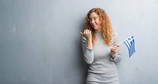 Young Redhead Woman Grey Grunge Wall Holding Flag Greece Pointing — Stock Photo, Image