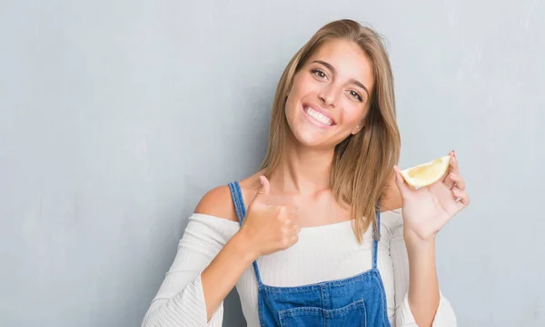 Krásná Mladá Žena Nad Grunge Šedá Zeď Drží Kousek Citronu — Stock fotografie