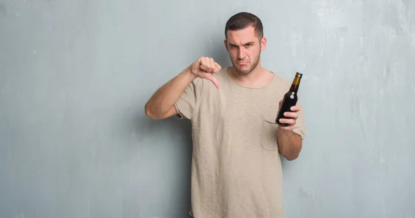 怒った顔 ダウン親指で嫌悪感を示すマイナス記号 拒絶反応の概念と瓶ビールを保持している灰色のグランジの壁を越えて若い白人男 — ストック写真