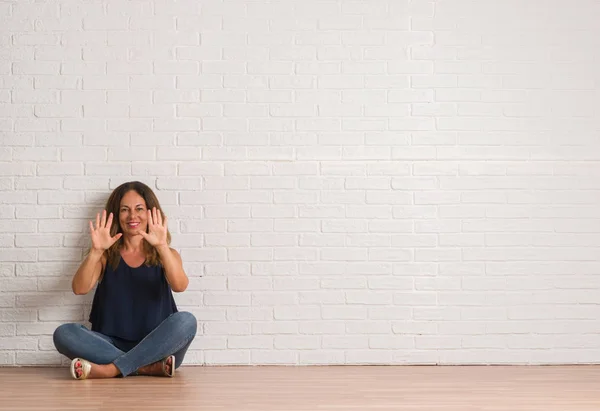 白いレンガの壁を示すと指で上向きに床に座っている中年のヒスパニック系女性は自信を持って 幸せな笑みを浮かべている間 数します — ストック写真