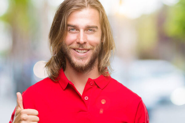 Young handsome man with long hair over isolated background doing happy thumbs up gesture with hand. Approving expression looking at the camera with showing success.