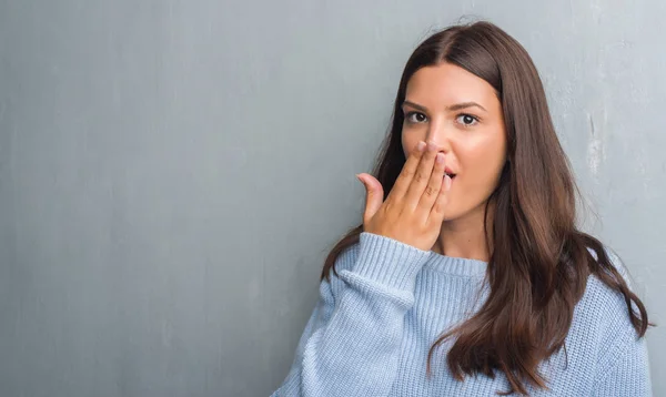 Young brunette woman over grunge grey wall cover mouth with hand shocked with shame for mistake, expression of fear, scared in silence, secret concept