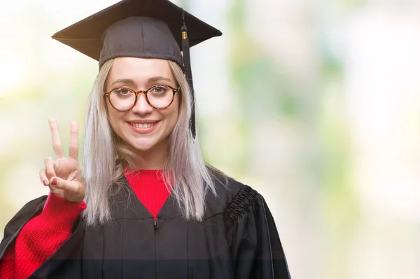 若いブロンドの女性の上の大学院の制服を着て分離で背景が表示され 自信を持って 幸せな笑みを浮かべている間 つ番号を指で上向き — ストック写真