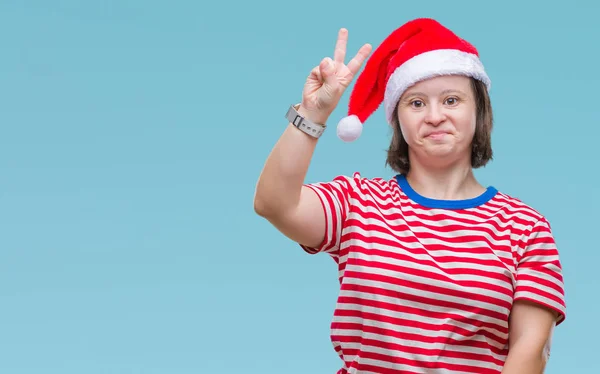 有唐氏综合症的年轻成年妇女戴着圣诞帽在与世隔绝的背景下微笑着 脸上带着快乐的面孔眨着眼睛做胜利的手势 第二个 — 图库照片