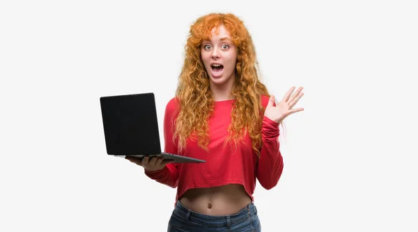 年轻红头发的妇女使用电脑笔记本电脑非常高兴和兴奋 优胜者表达庆祝胜利尖叫着大微笑和举手 — 图库照片