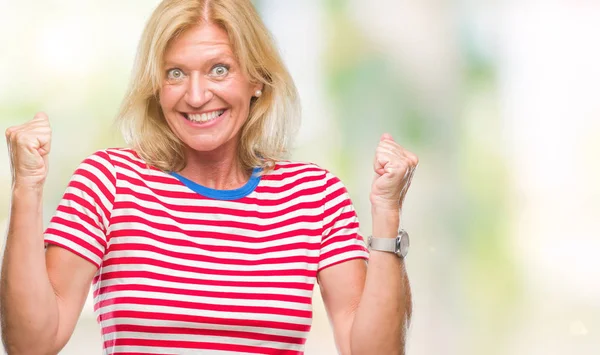 Orta yaş sarışın kadın kutluyor izole arka plan üzerinde şaşırttı ve başarı için kaldırdı kollarını açarak hayret ve gözleri açık. Kazanan kavramı.