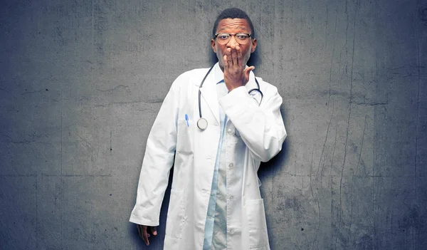 Young black doctor, medical professional covers mouth in shock, looks shy, expressing silence and mistake concepts, scared