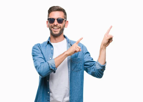 笑顔で側に つの手と指で指しているカメラを見て孤立の背景の上にサングラスをかけている若いハンサムな男 — ストック写真