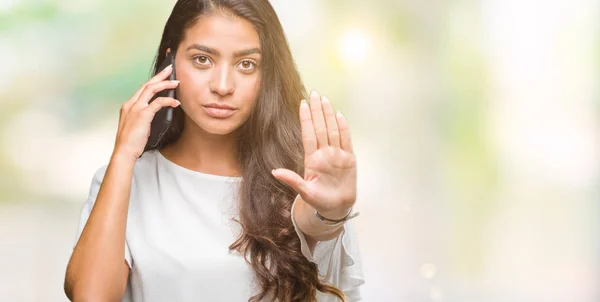 年轻美丽的阿拉伯妇女在电话上谈论孤立的背景与张开手做停止标志认真和自信的表达 防御姿态 — 图库照片