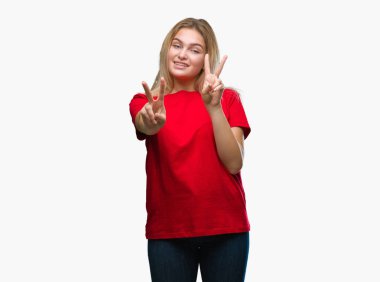 Zafer işareti yapıyor parmak gösterilen kamera seyir gülümseyen izole arka plan üzerinde beyaz kadın. İki numaralı.