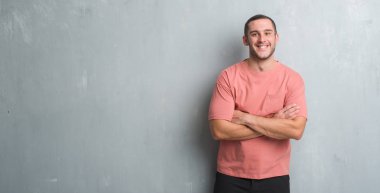 Üzerinde gri grunge Duvar ile mutlu yüz gülümseyen Genç beyaz adam kameraya seyir silah geçti. Olumlu bir kişi.