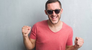 Duygu tezahürat Genç beyaz adam gurur çığlık ve zafer ve başarı çok heyecanlı, kutluyor güneş gözlüğü takıyor gri grunge duvarın üzerinden