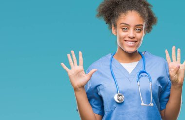 Genç afro Amerikalı doktor kadın gösterilen ve parmakları ile işaret izole arka plan üzerinde numara 9 kendinden emin ve mutlu gülümseyerek süre.