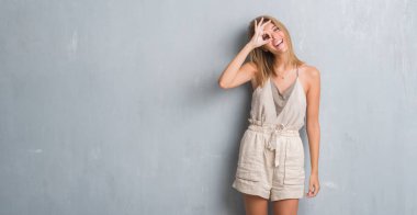 Güzel genç kadın mutlu yüz el parmaklarının arasından seyir göz üzerinde ok işaretiyle yapıyor gülümseyen grunge gri duvardan ayakta