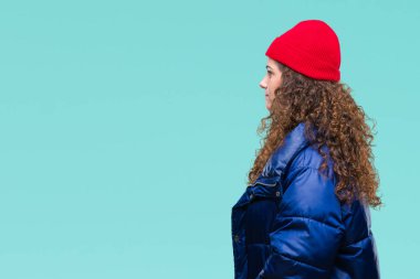 Güzel genç esmer kıvırcık saçlı kız tarafına, seyir izole arka plan üzerinde kış ceket, yün kap ve kazak giyiyor dinlenmek doğal yüz emin gülümseme ile pozuyla profil.