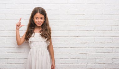 Beyaz tuğla duvar gülümseyen ve süre seyir ve kamera boyutu işaret parmaklarıyla yapıyor el ile kendinden emin eller genç İspanyol çocuk. Ölçü kavramı.