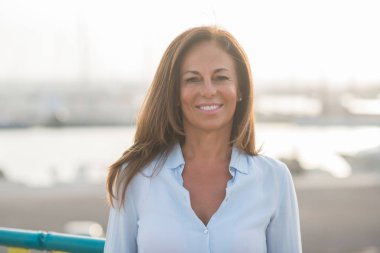 Street yüzünde gülümseme ile duran güzel orta yaş İspanyol kadın. Şehir gezinti güvenli ve neşeli güneşli bir günde gülümseyen denizin kenarında yürüyüş.