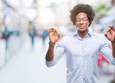 Afro Amerikan iş adam gözlük izole arka plan üzerinde dinlenmek ve gülümseyen gözlerle kapalı parmak jestle meditasyon yapıyor. Yoga kavramı.