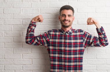 Kol kasları gururlu gülümseyen gösterilen beyaz tuğla duvardan ayakta genç yetişkin adam. Fitness kavramı.