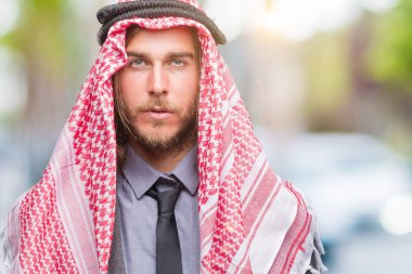 Genç yakışıklı Arap adam uzun saçlı yüzünde ciddi bir ifade ile izole arka plan üzerinde keffiyeh giyiyor. Basit ve doğal kameraya bakıyor.