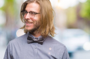 Genç yakışıklı adam uzun saçlı uzak tarafına yüzünde, doğal ifade gülümseme ile seyir izole arka plan üzerinde papyon giyiyor. Kendine güvenen gülüyor.