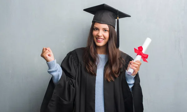 Joven Morena Sobre Pared Gris Grunge Vistiendo Uniforme Graduado Sosteniendo — Foto de Stock