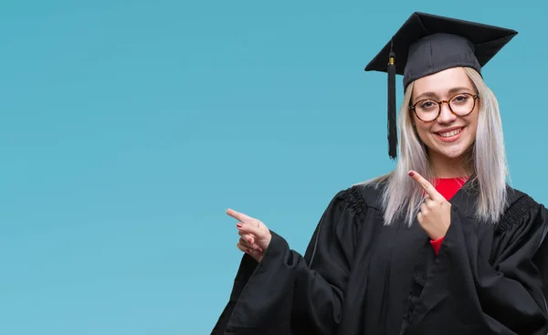 笑顔で側に つの手と指で指しているカメラを見て孤立の背景に大学院の制服を着て若いブロンドの女性 — ストック写真