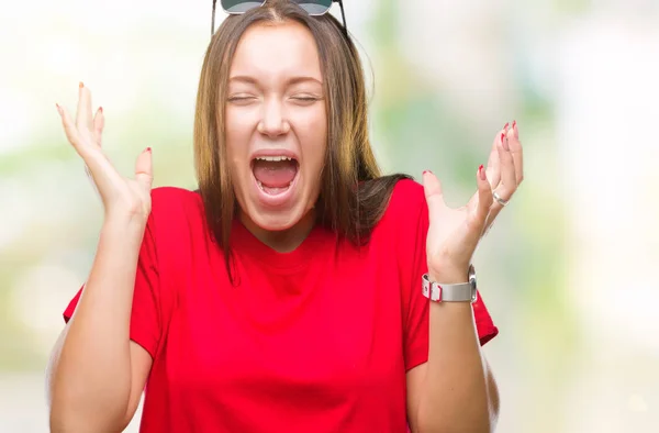 年轻美丽的高加索妇女戴着太阳镜在孤立的背景庆祝疯狂和惊讶的成功与手臂抬起和睁开眼睛尖叫兴奋 优胜者概念 — 图库照片