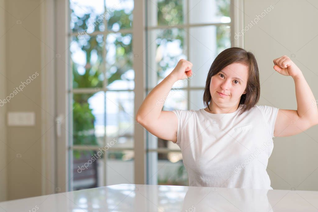 Down syndrome woman at home showing arms muscles smiling proud. Fitness concept.