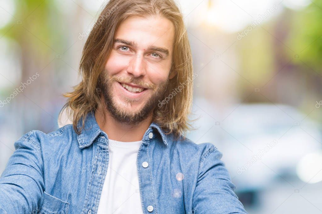Young handsome man with long hair over isolated background looking at the camera smiling with open arms for hug. Cheerful expression embracing happiness.